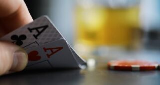 Beste Poker Starthände beim Texas Hold’em: Zwei Asse in der Hand eines Spielers neben Pokerchips und einem Getränk im unscharfen Hintergrund.