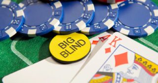 Ein Big-Blind-Button liegt auf Spielkarten mit Ass und König in Karo, daneben liegen blaue Pokerchips auf grünem Filz.