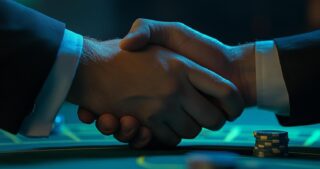 Zwei Personen geben sich über dem Pokertisch die Hand, neben ihnen liegen Chips, und die Szene symbolisiert Collusion beim Poker.