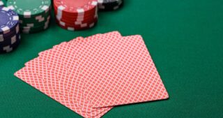 Mehrere verdeckte Spielkarten liegen fächerförmig als Muck-Stapel auf grünem Pokertisch, daneben sind unscharfe Pokerchips zu sehen.