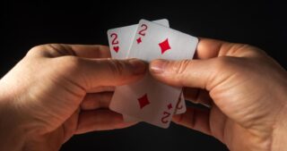 Zwei Hände halten ein Kartenpaar aus zwei Zweien, Herz und Karo, vor dunklem Hintergrund und veranschaulichen ein Pair beim Poker.