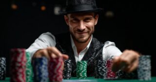 Ein lächelnder Pokerspieler mit Hut greift nach mehreren Stapeln bunter Chips am Tisch und symbolisiert ein Re-Raise beim Poker.