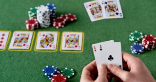 Ein Spieler hält zwei Asse in der Hand, während Karten und Pokerchips auf dem grünen Tisch liegen und die Szene einen Suckout beim Poker zeigt.