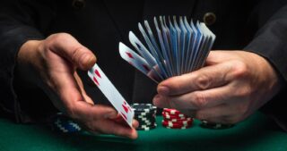 Wrap beim Poker: Spielerhände halten aufgefächerte Spielkarten über einem grünen Pokertisch, daneben liegen Pokerchips in dramatischem Licht.